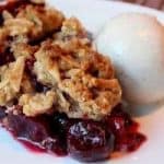 Bowl of cherry pie with crumbs on the top with ice cream on the side