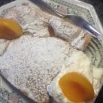 An Apricot Sponge Slice placed on a silver platter with a fork on the side. Slice dusted with icing sugar