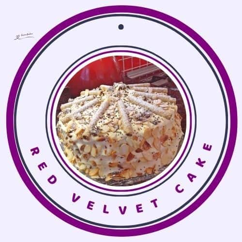 an image of a Red Velvet Cake with cream cheese frosting and decorated with slivered almonds and chocolate curls