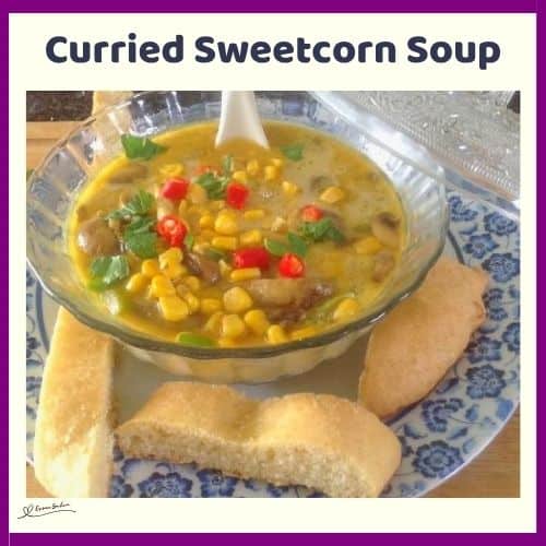 an image of a glass bowl with Curried Sweetcorn Soup and bread on the side