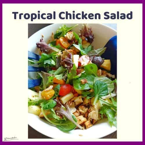 an image of a Tropical Chicken Salad in a white bowl with blue salad utensils