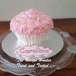 A pink Basic Cream Cheese Frosting on a white cupcake with a light pink cutout with the name Caroline written in pink frosting on a white background