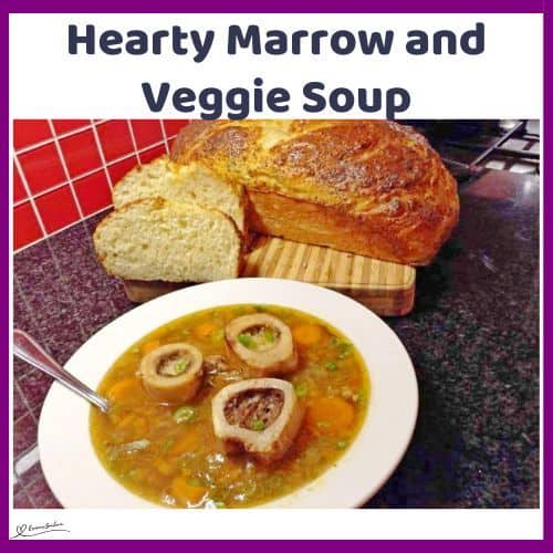 an image of a white soup bowl filled with Hearty Marrow and Veggie Soup and bread on the side