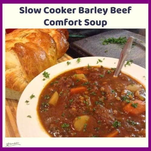 An image of a bowl of Slow Cooker Barley Beef Comfort Soup with fresh bread on the side