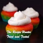 3 rainbow cupcakes with blue, green, yellow and orange segments and white cream to top it off
