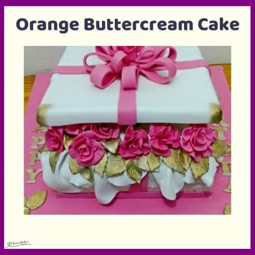 An image of an orange buttercream cake in the shape of a gift with a pink bow and pink roses between the layers