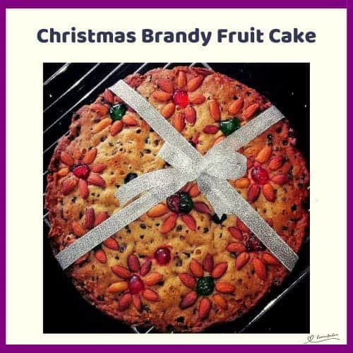 An image of a Christmas Brandy Fruit Cake Decorated with Nuts, Cherries and a Ribbon
