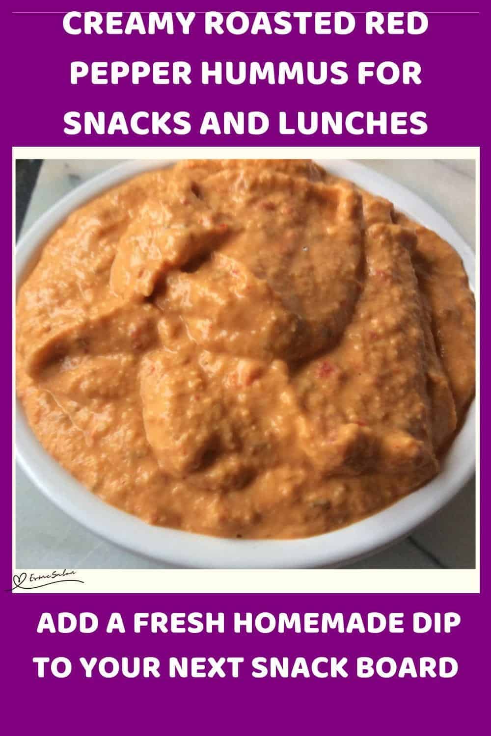 An image of a white bowl filled with Creamy Roasted Red Pepper Hummus with toasted bread triangles and carrots on the side