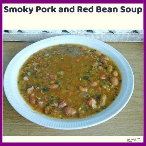 An image of a white bowl of Smoky Pork and Red Bean Soup with loads of vegetables and pork rashers