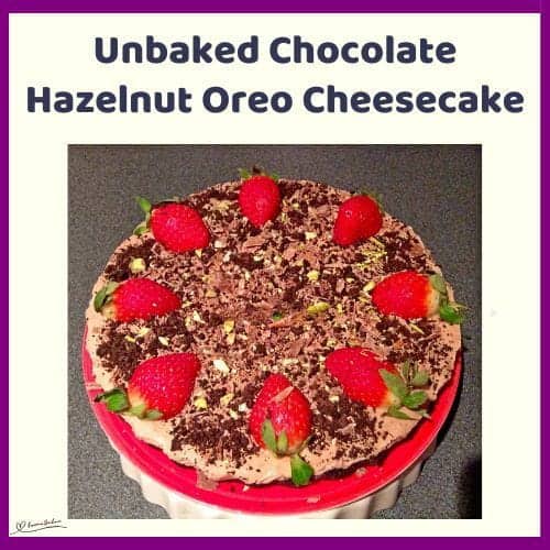 An image of a round Unbaked Chocolate Hazelnut Oreo Cheesecake decorated with strawberries, pistachios, Toblerone shavings, and the crushed Oreo biscuits