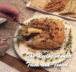 Brie cheese baked in a dough casingon a white platter sliced