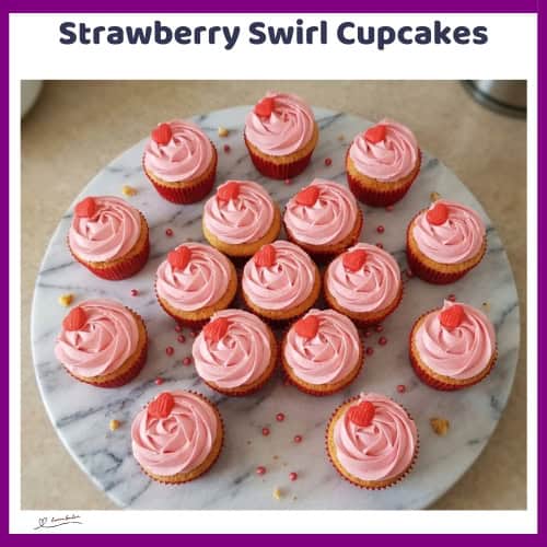An image of a box and side plate with Strawberry Swirl Cupcakes with pink frosting and a small red heart as decoration