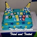 A blue square birthday cake with two banana people in pajamas for a 1-year old's birthday cake