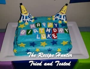 A blue square birthday cake with two banana people in pajamas for a 1-year old's birthday cake