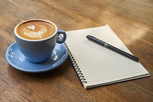 Blue cup with coffee, a writing pad and pen on a wooden table