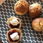 two half scones with jam and cream and 3 full scones on a blue plate