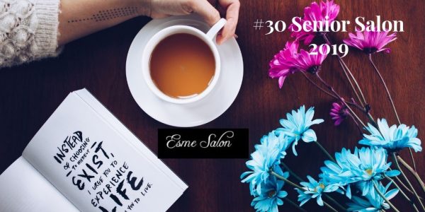 Hand holding a cup of chocolate drink next to blue and pink flowers