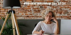 elderly lady writing in her notebook sitting on a grey chair, a black stand lamp and green plant on table