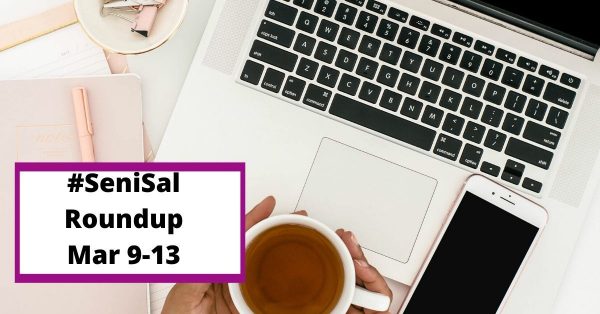 hands holding a cup of black tea, an iPhone on the keyboard of a laptop with pink pen and notepad on the side