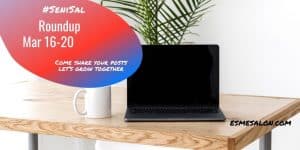 black laptop, white mug on a brown wooden table and green foliage as backdrop