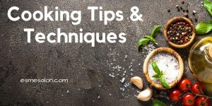 wooden bowls with salt, pepper corns, tomatoes and garlic on a black surface