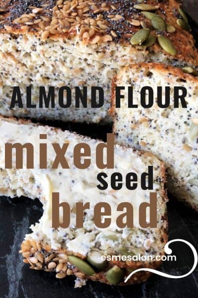 Almond Flour seed bread with a line of pepitas, black poppy seed and sesame seeds covering the top and a buttered slice of bread from which a piece eaten