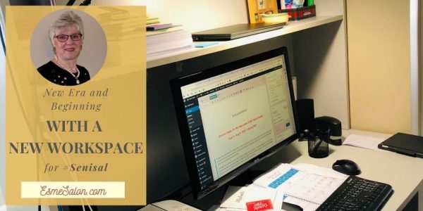 Image of Esme's workspace - large wooden desk, with black screen and keyboard and shelving housing paperwork and other stationary