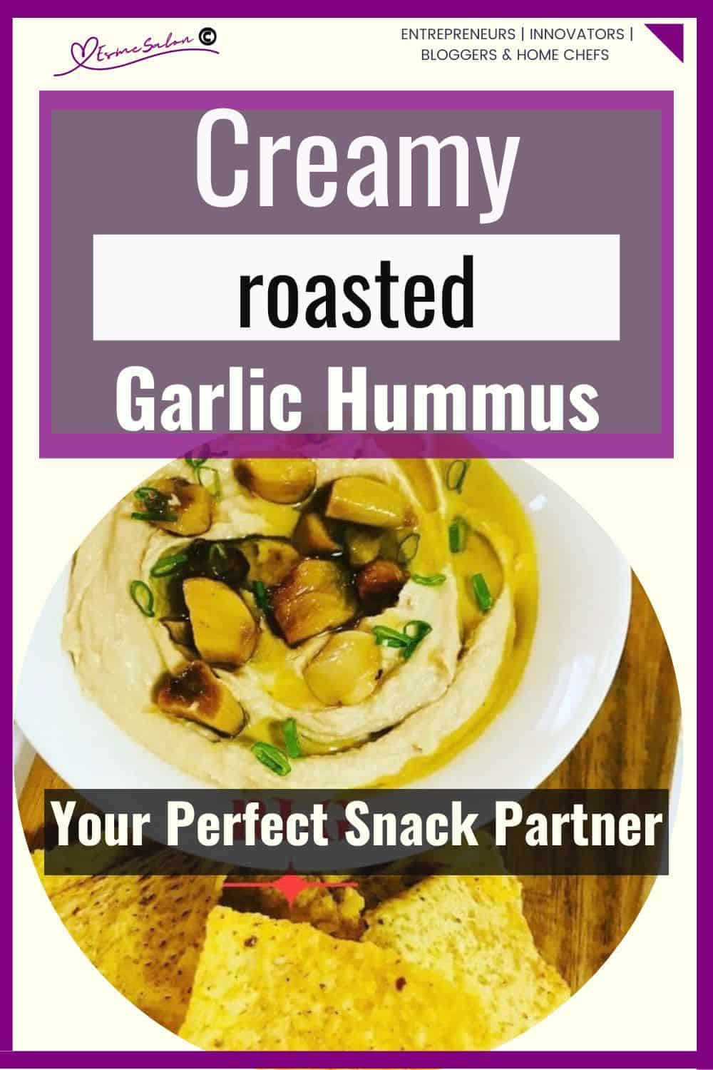 an image of a white bowl filled with Creamy Garlic Roasted Hummus on wooden table with some crisps as well