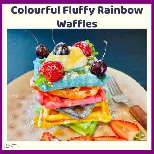 An image of a stack of colourful, fluffy, rainbow waffles with fruit and some cherries