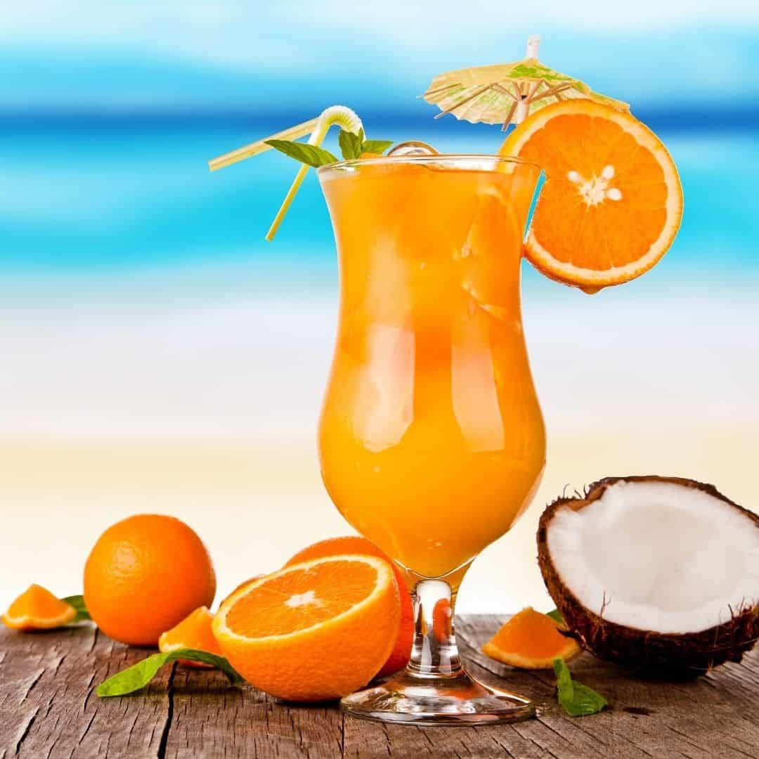 An image of a tall glass of orange juice on a wooden table with a half of coconut on the side