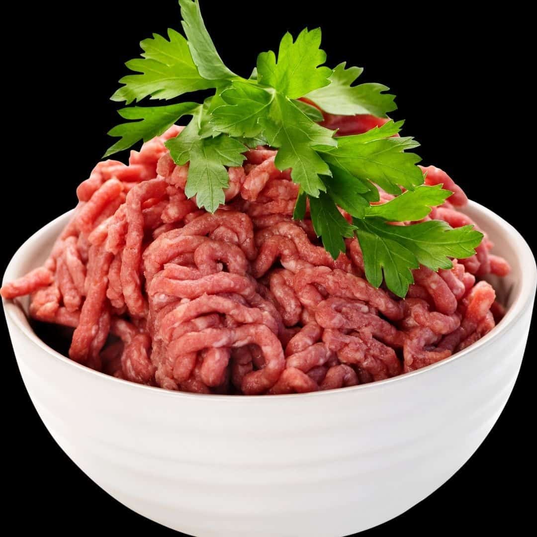 An image of ground beef in a white bowl with broad leave parsley