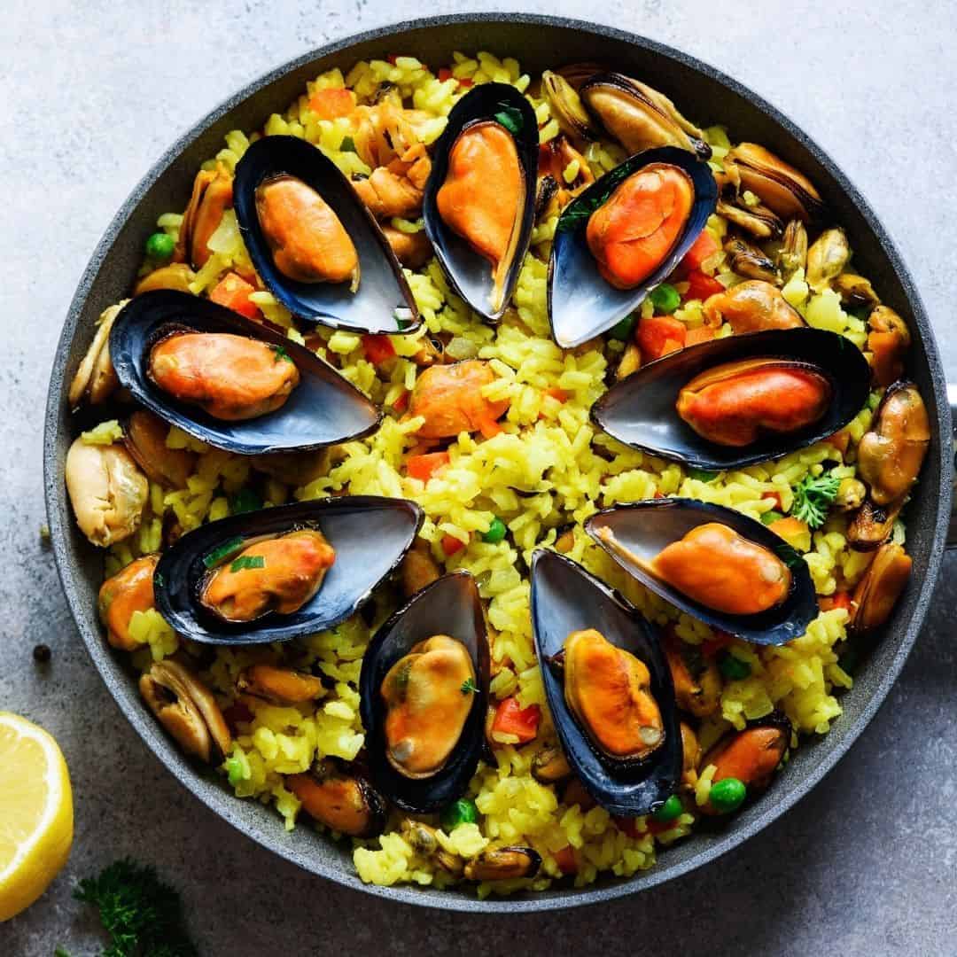 An image of a deep dish filled with yellow rice and mussels in the shell