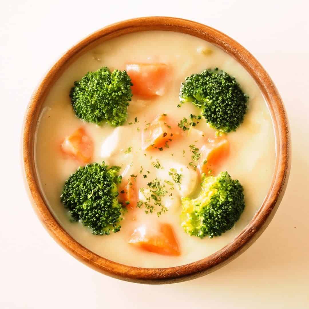 An image of a ceramic brown bowl with creamy soup with carrots and broccolli