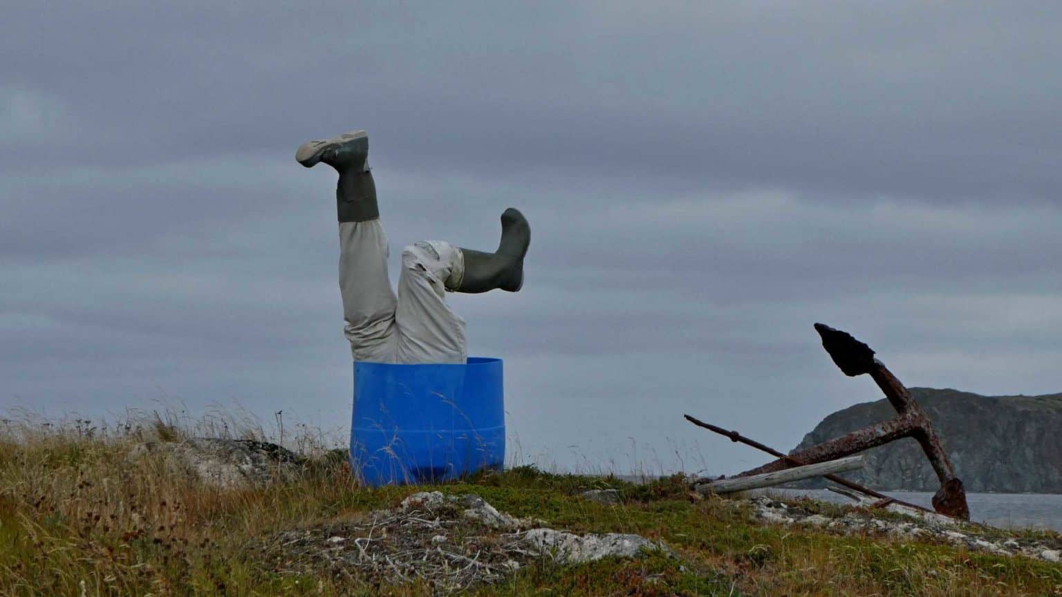 an image of a blue bucket and what seems to be a man that fell in the bucket head first and only his legs and feet sticking out