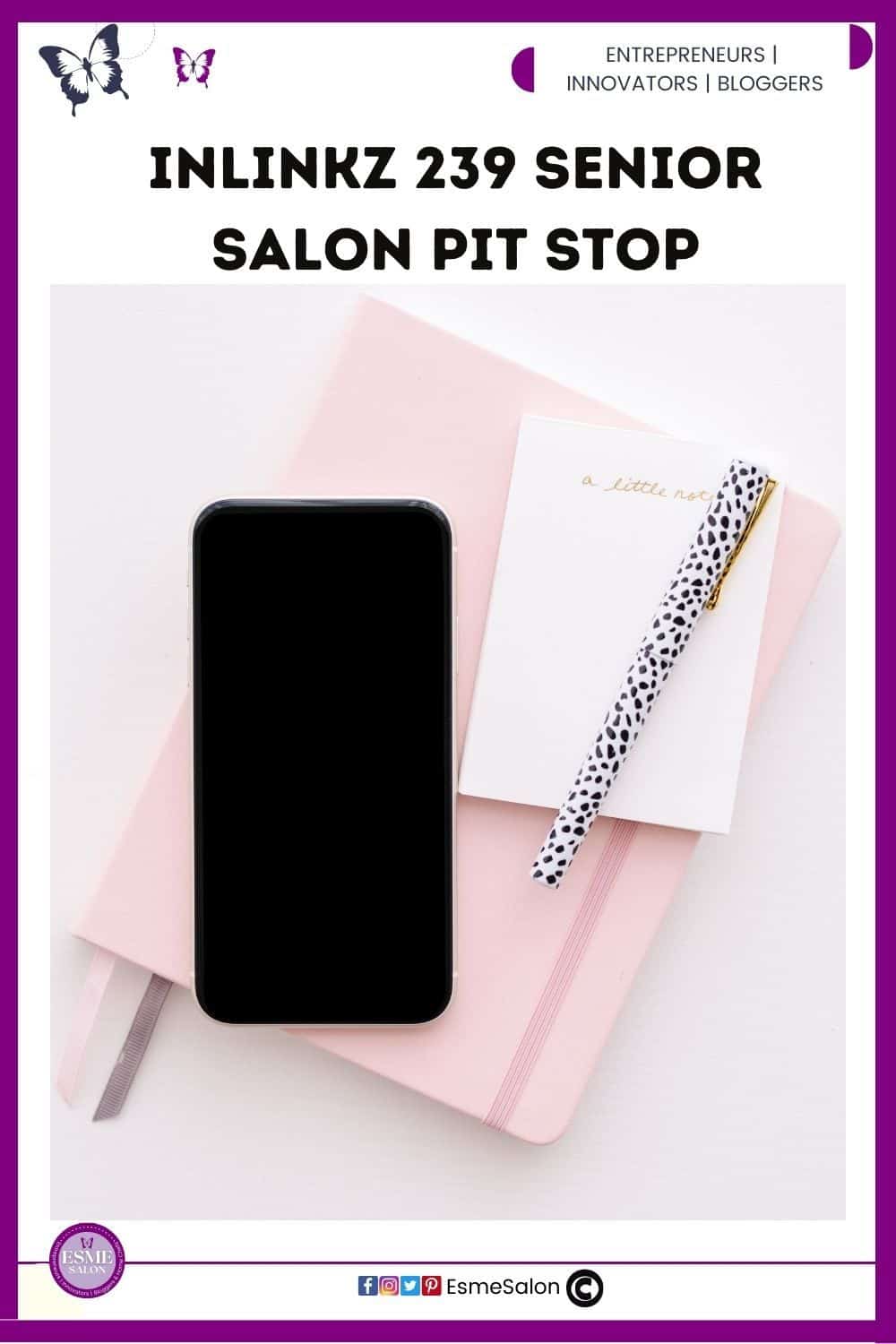 an image of a white desk, with a pink notebook and on top of that a black screen mobile phone with a leopard print pencil on the side