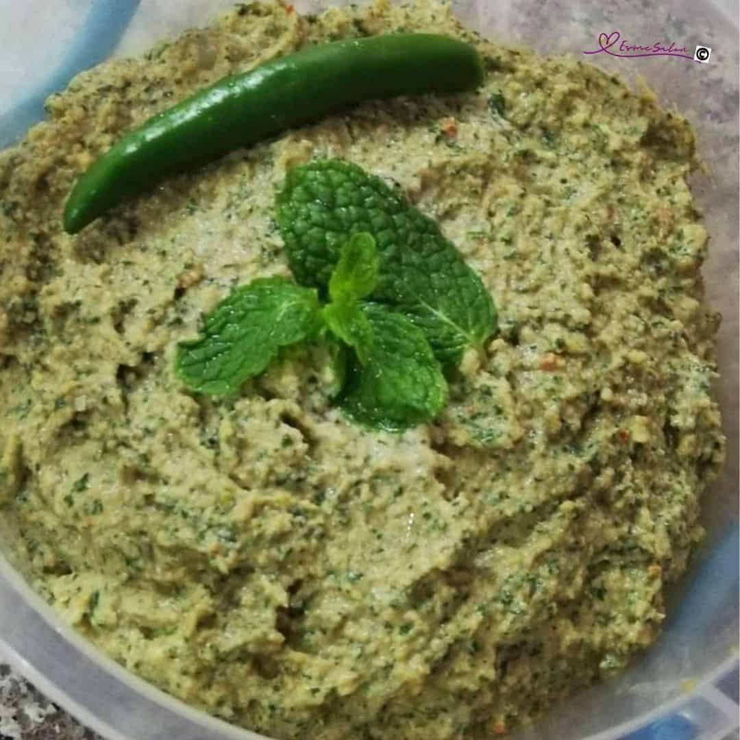an image of a plastic container filled with Vegan Mint Chutney and a mint leave as decoration
