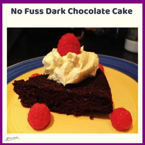 An image of a No Fuss Dark Chocolate Cake with a small dollop of cream and a few raspberries